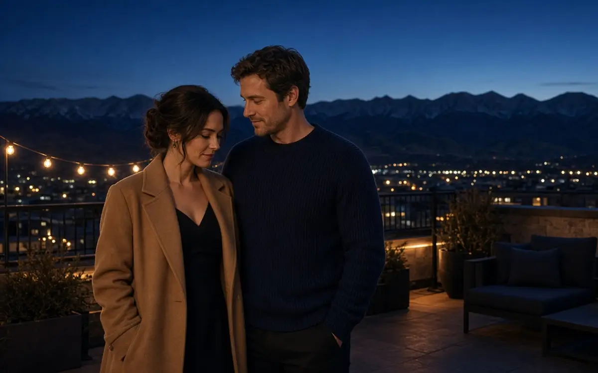 A dressed couple on a Denver rooftop at dusk, her camel coat and the mountains behind them.
