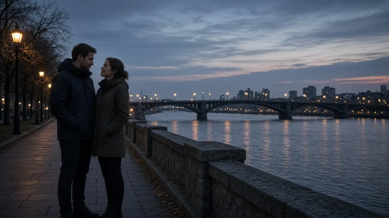 A dressed couple on a riverfront sidewalk at dusk, a bridge and warm street lamps.